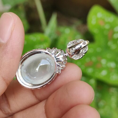 a hand holding a silver pendant with a clear stone in it