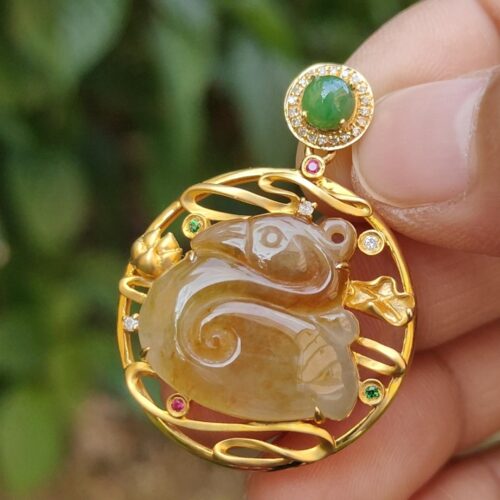a hand holding a gold pendant with a jade and gemstone