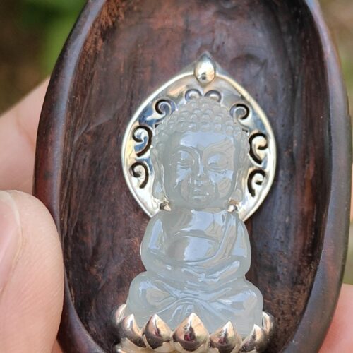 a hand holding a carved wooden spoon with a carved stone statue