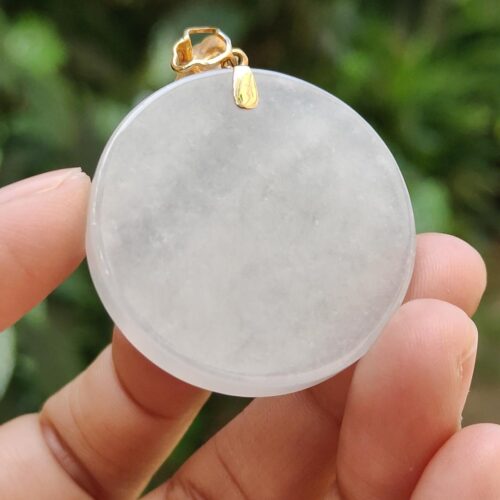 Una mano sosteniendo un colgante de piedra blanca redonda.