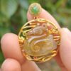 a hand holding a gold pendant with a jade and gemstone