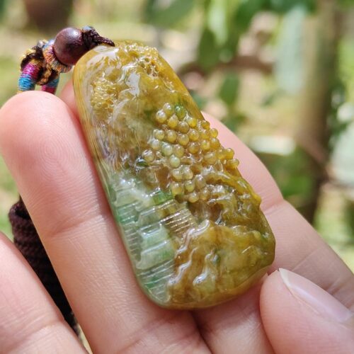 a hand holding a yellow and green stone pendant