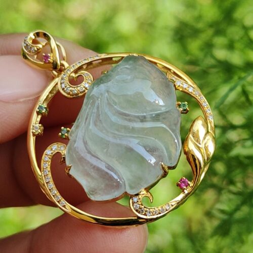 a hand holding a gold pendant with a jade stone and diamonds
