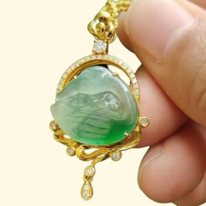 a hand holding a gold necklace with a jade pendant