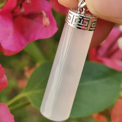 a hand holding a white cylinder necklace