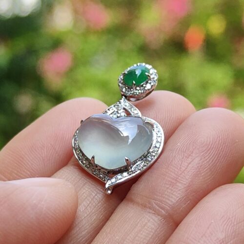 a hand holding a silver heart shaped ring with a green stone