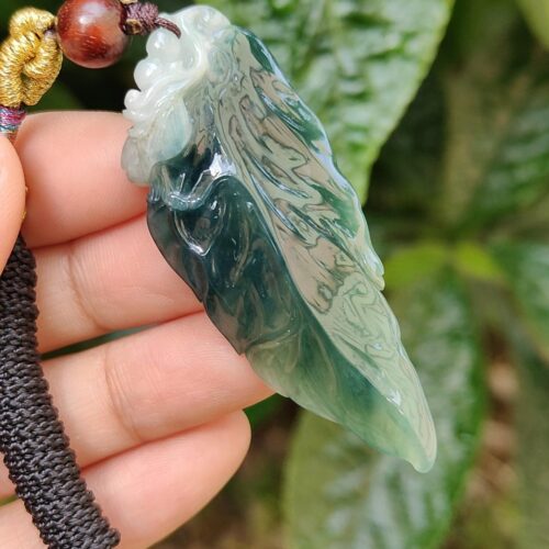 a hand holding a jade leaf pendant