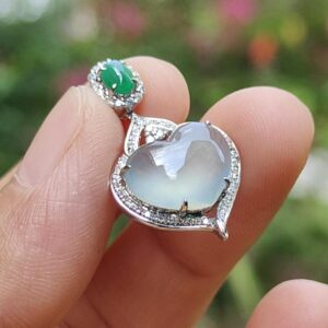 eine Hand, die einen silbernen herzförmigen Ring und einen grünen Stein hält