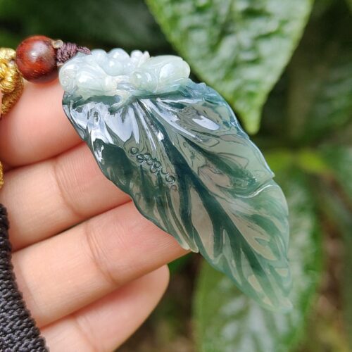 a hand holding a jade leaf pendant
