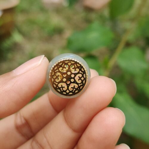 a hand holding a round object with a gold design