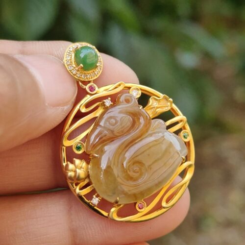 a hand holding a gold pendant with a stone swan