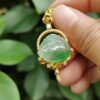 a hand holding a gold necklace with a green stone in the center