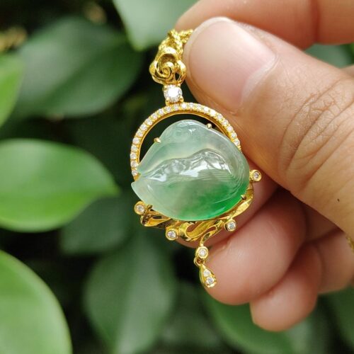 a hand holding a gold necklace with a green stone in the center