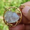 a hand holding a gold pendant with a stone in the center