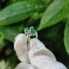 a hand holding a silver ring with green stones