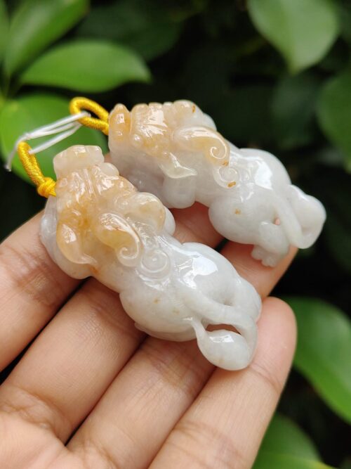 a hand holding a pair of white and orange carved elephants