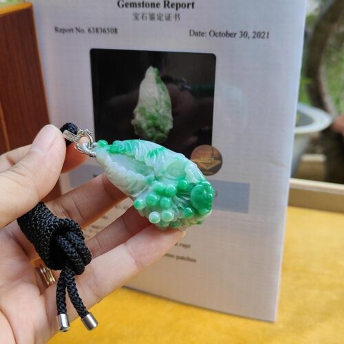 a hand holding a green and white stone pendant