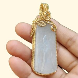 a hand holding a gold and white stone pendant