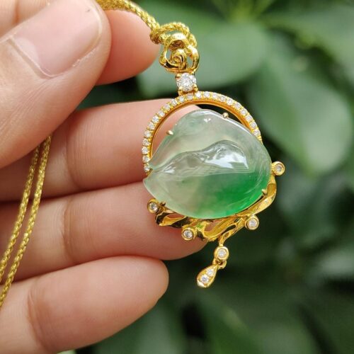 a hand holding a gold necklace with a green stone in the center