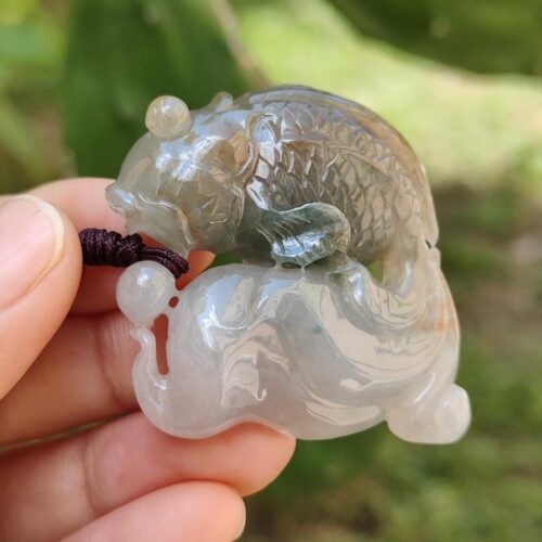 a hand holding a jade fish pendant