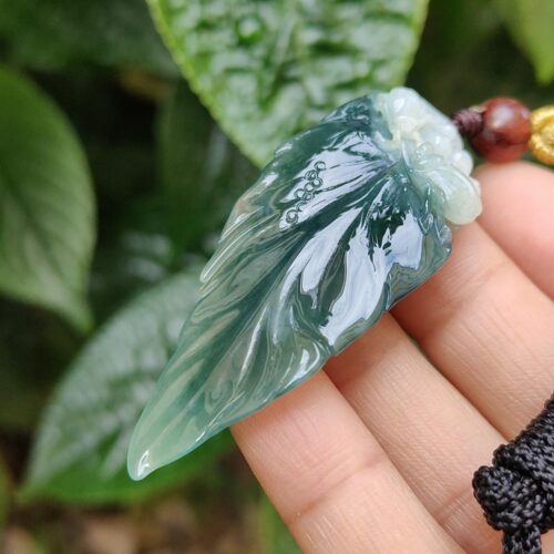 a hand holding a green and white leaf pendant