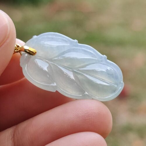 a hand holding a jade leaf pendant