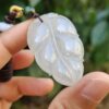 a hand holding a jade leaf necklace