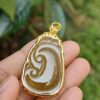 a hand holding a gold and white pendant