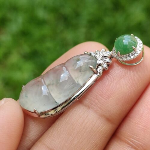 a hand holding a silver pendant with a green stone on it