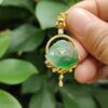 a hand holding a gold necklace with a green stone in the middle