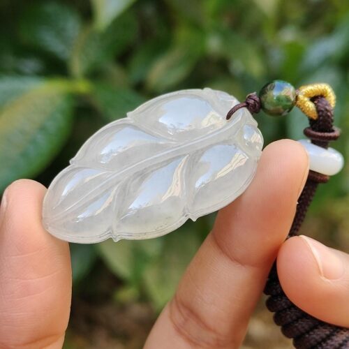 a hand holding a jade leaf pendant
