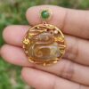 a hand holding a gold pendant with a green and red stone