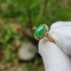 a hand wearing a white glove holding a ring with a green stone