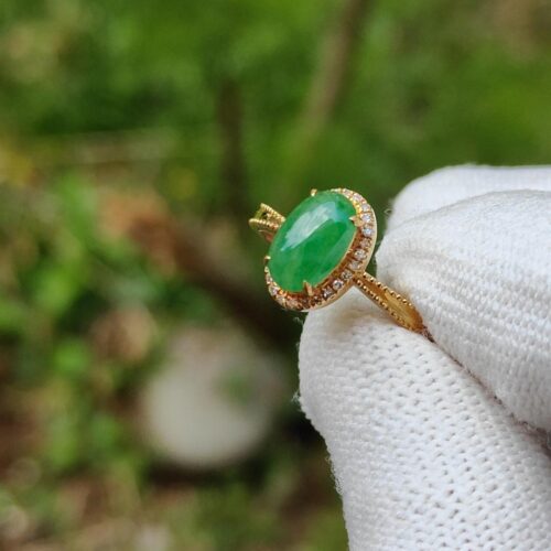 a hand wearing a white glove holding a ring with a green stone
