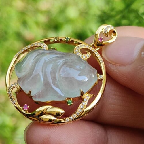 a hand holding a gold pendant with a jade stone in it