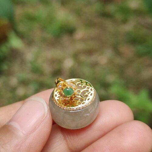 a hand holding a small round object with a gold and green stone