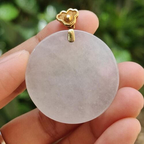 Una mano sosteniendo un colgante de piedra blanca redonda.