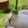 a hand wearing a gold ring with a green stone