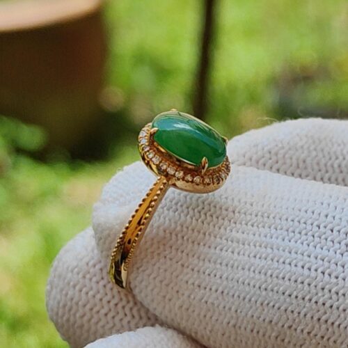 a hand wearing a gold ring with a green stone