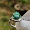 a hand wearing a gloved hand holding a ring with a green stone