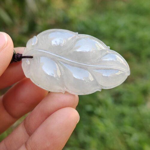 a hand holding a white jade leaf pendant