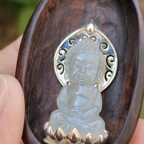 a hand holding a carved wooden spoon with a carved buddha statue