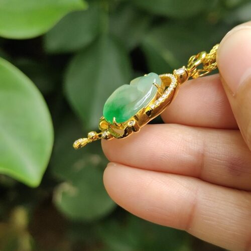a hand holding a gold necklace with a green stone