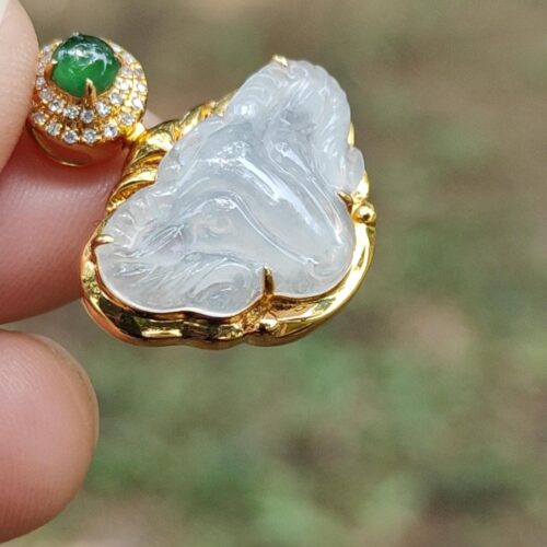 a hand holding a gold pendant with a jade and diamond