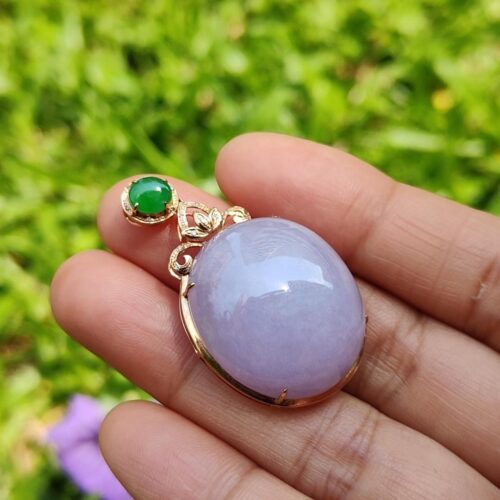 a hand holding a purple and green stone pendant