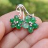 a hand holding a silver earrings with green stones