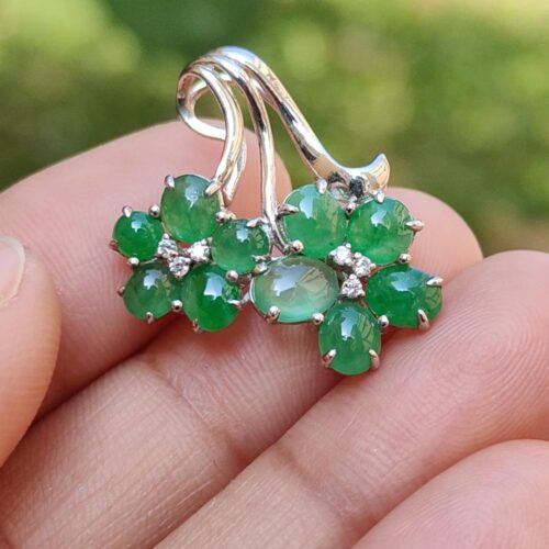 a hand holding a silver earrings with green stones