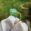 a hand holding a gold ring with a jade stone