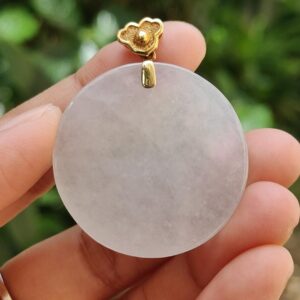 Una mano sosteniendo un colgante de piedra blanca redonda.