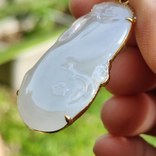 a hand holding a white jade pendant